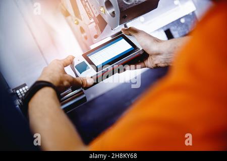 Industrial worker measures roughness and frequency of machined part after lathe with instrument. Stock Photo