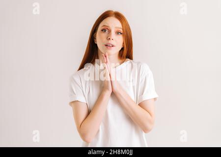 Portrait of desperate young woman makes imploring expression keeps palms pressed together asks for favor says please looking at camera with hope. Stock Photo