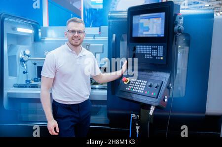 Happy Industrial worker man in glasses operating CNC laser turning machine at automatic modern factory floor. Stock Photo