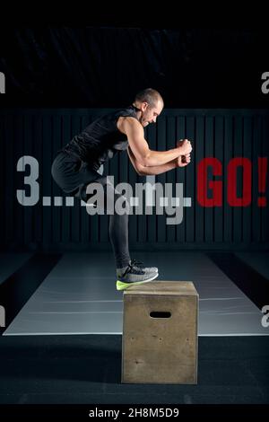 Athlete gave exercise. Jumping on the box. Phase touchdown. Studio shots in the dark tone. Stock Photo