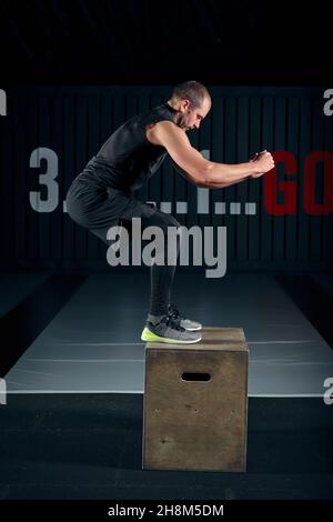 Athlete gave exercise. Jumping on the box. Phase touchdown. Studio shots in the dark tone. Stock Photo
