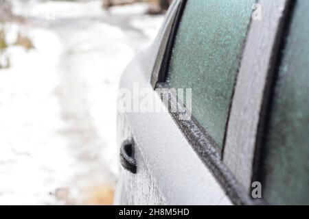 A close-up of a frozen car door, car window covered with ice. Unfreezing, de-icing the car door properly to open frozen car locks, doors and windows d Stock Photo
