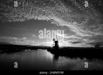 A monochrome image of the River Ant on the Norfolk Broads with iconic windmill and detailed sky in an autumn sunset at Ludham, Norfolk, England, UK. Stock Photo
