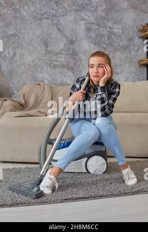 Young woman with cleaning equipment ready to clean house, sitting on couch. Fatigue Stock Photo