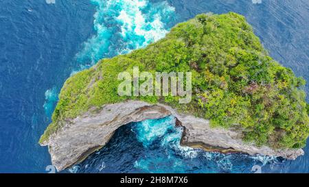 Aerial top view by drone of ocean blue waves break on high cliff of a rocky mountain. Waves crash into the bank of a stony cliff with a crack in the Stock Photo