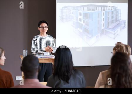 Asian businesswoman in eyeglasses presenting her report for people at the seminar, she talking about the blueprint of modern building Stock Photo