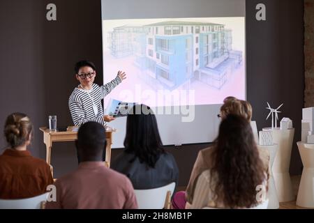 Asian young man in eyeglasses pointing at whiteboard with modern building and explaining the blueprint for business people at seminar Stock Photo