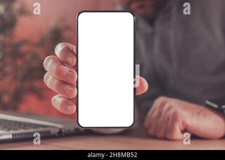 Mock up blank screen of modern smart phone in male hands over laptop computer, freelancer using mobile phone, top view Stock Photo