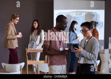 Colleagues using mobile phone and talking to each other during a break at business seminar Stock Photo