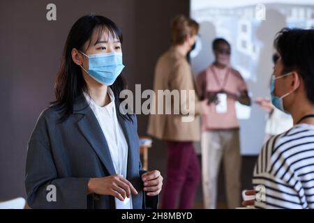 Two businesswomen in protective masks talking to each other while visiting business seminar Stock Photo