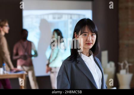 Portrait of Asian young businesswoman looking at camera while standing in the boardroom with other business people Stock Photo