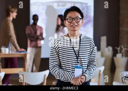 Portrait of Asian businesswoman in eyeglasses smiling at camera while visiting business seminar Stock Photo