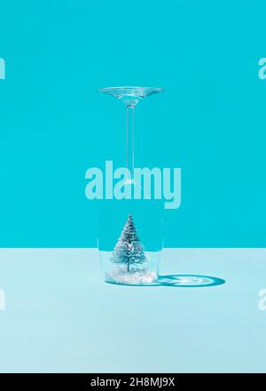 Christmas tree in the snow inside a wine glass against blue background. Minimal concept Stock Photo