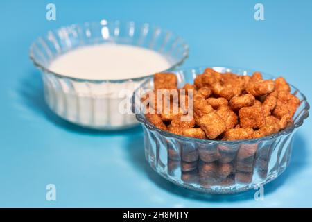 Glass bowls with chocolate flavored corn flakes and milk on blue background Stock Photo