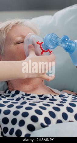 Close up of hyperventilating woman in hospital ward bed while doctor and nurse using oxygen tube for respiratory problem. Senior patient receiving help against breathing heavily. Stock Photo