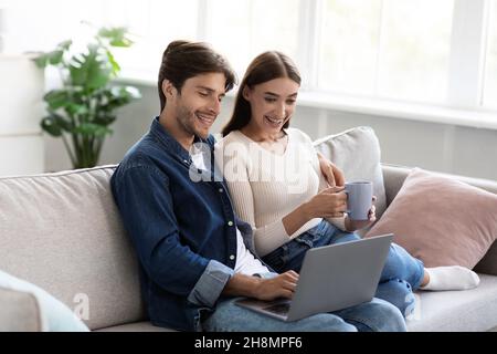 Cheerful millennial european husband and wife spending free time and weekend together, looking at laptop Stock Photo