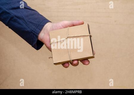 An adult male is holding a brown gift box in his hand. The rectangular cardboard box is tied with string. Close-up. Selective focus. Stock Photo