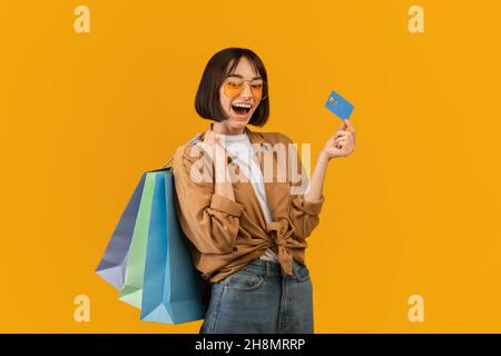 Easy shopping concept. Excited woman holding credit card and shopper bags and looking at camera with open mouth Stock Photo