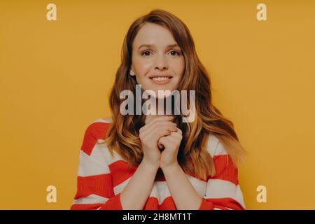 Young happy woman feeling grateful, thankful and blessed while standing against yellow wall Stock Photo