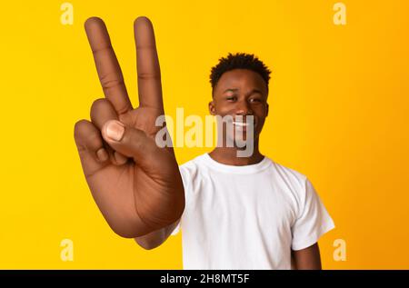 Young African American guy smiling at camera and showing big peace or victory gesture over orange background Stock Photo