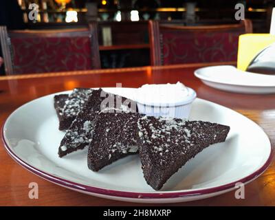 Black bread croutons with garlic. Beer snack. Fried rye bread sprinkled with garlic and sauce on a ceramic plate on a table in a pub. Stock Photo