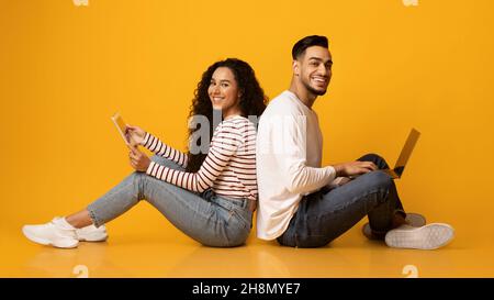 Cheerful arab couple sitting back to back with laptop and digital tablet Stock Photo