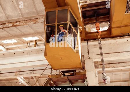 Male worker sitting in operator cabin of overhead crane Stock Photo