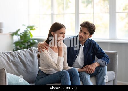Serious careful young european guy calms upset unhappy lady in living room interior Stock Photo