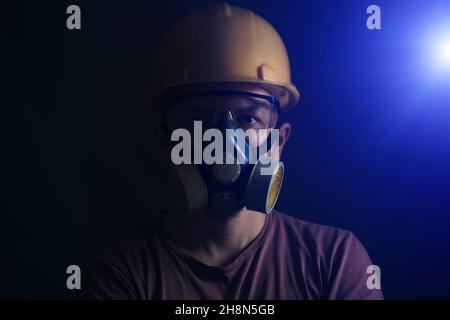 Portrait miner in protective helmet, glasses and respirator, with bright spotlight Stock Photo