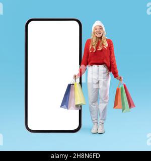 Female customer posing with white empty smartphone screen holding bags Stock Photo
