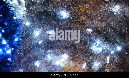 Close-up of tinsel with garland. Concept. Blue garland glows in silvery glittering tinsel. Christmas decorations. Beautiful bright holiday decorations Stock Photo