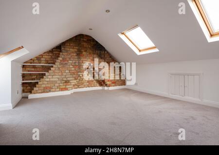 Cambridgeshire, England - November 4 2019: Cottage attic loft space converted into a bedroom with roof light windows and exposed brickwork Stock Photo