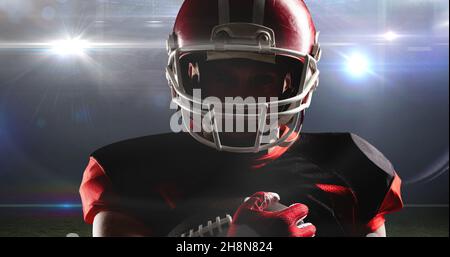 Portrait of male american footballer holding ball at illuminated sports field Stock Photo