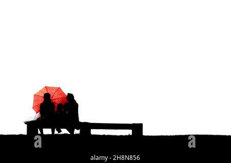 Silhouette of parents with child behind umberella sitting on bench Stock Photo