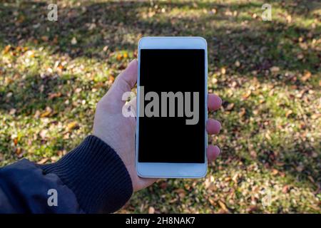 Mockup image of man hand holding white mobile phone with blank black screen on the nature background. Stock Photo