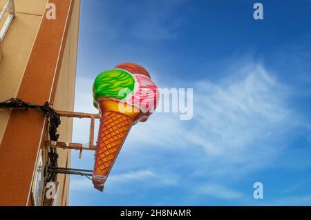 Big plastic Ice cream cone sign in the street outside a shop with blue sunny sky. Stock Photo