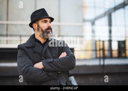 Portrait of businessman in black clothing standing in front of company building. Black bearded man is wearing winter clothing. Stock Photo