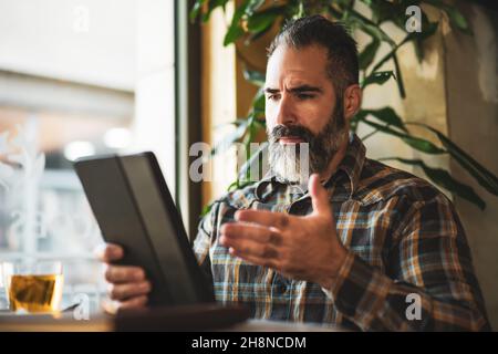 Adult man is sitting in cafe and using digital tablet. Stock Photo