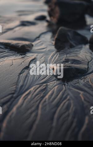 Close up macro shot of wet sand on the beach. Black dark sand with rocks in it. Lines in the sand. Vertical Stock Photo