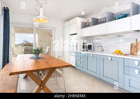 Combination of classic and modern kitchen  in white and blue color with wooden dining set Stock Photo
