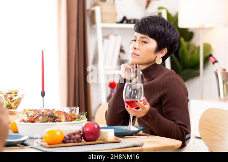 Happy young asian woman holding wineglass and drinking at home in Christmas day, thanksgiving eve, family with female sitting cozy on food table for r Stock Photo