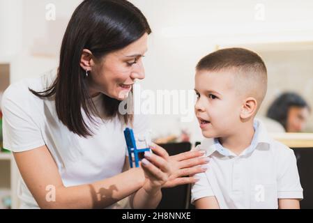 A beautiful woman speech therapist deals with the boy and teaches him the correct pronunciation and competent speech. Stock Photo