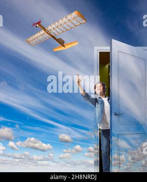 A teenager in a helmet of pilot opening the door his room to the sky and launches a model plane to the flight. The boy dreams of becoming a pilot. Stock Photo