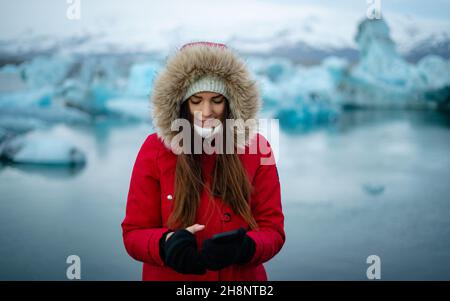 Cute girl traveler in winter at Jokulsarlon Glacial Lagoon during their vacation in nature, female tourist uses mobile phone while enjoying vacation Stock Photo