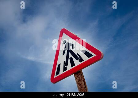 Pedestrian crossing sign against a blue sky, red triangle. Stock Photo