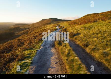 Cold autumn sunrise on a frost covered path heading towards Higger Tor high in the Derbyshire Peak District. Stock Photo