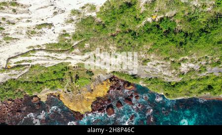 Extremely dangerous footpath on a cliff wall to Seganing Waterfall. Rocky cliff shore and hiking trail on mountain near Kelingking beach. Aerial view Stock Photo