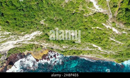 Extremely dangerous footpath on a cliff wall to Seganing Waterfall. Rocky cliff shore and hiking trail on mountain near Kelingking beach. Aerial view Stock Photo