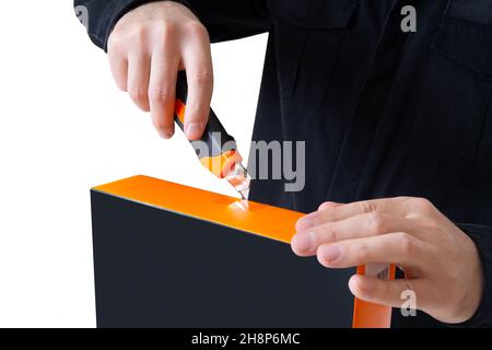 Man in black uniform opening a product box with a utility knife. Stock Photo