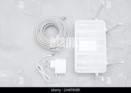 Top view of a Wi-Fi 6 router with a power supply adapter and a roll of ethernet cable on a concrete table Stock Photo